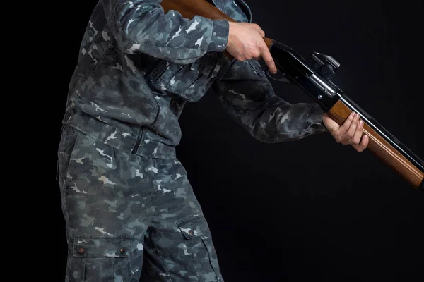 Militär eller jägare med ett hagelgevär. En man som håller en pistol med en syn. Man i Arméuniform. Soldat, trooper på en svart bakgrund. En man med en pistol i kamouflage militär uniform. — Stockfoto