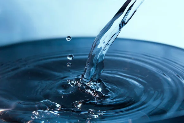 Blå ström av vatten på en ljus bakgrund. Vatten som strömmar in i en stor skål. — Stockfoto