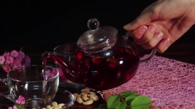Çaydanlıktan bardağa çay dök. Kırmızı çay ve yapraklardan oluşan yaratıcı bir düzen. Çay saati: çay, çarşaf, karkade, rooibos. Doğulu, rahat, tören, gelenek, Japon, yapraklı