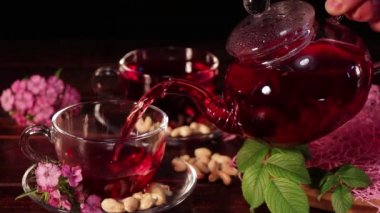 Çaydanlıktan çay dök ve cam bardaktan iç. Cam bardakta kırmızı amber çayı. Çay saati: çay, çarşaf, karkade, rooibos. Doğulu, samimi, tören, gelenek, Japonca, yapraklı, hygge
