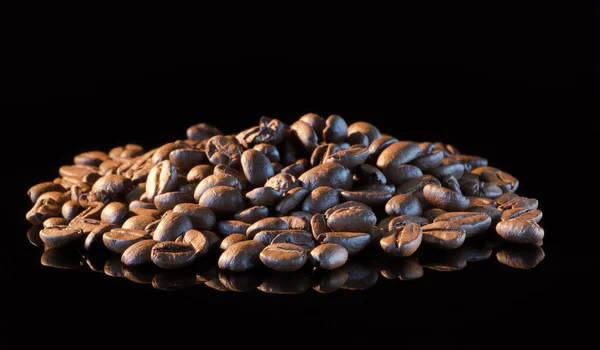 Coffee beans on a black mirror background close-up.