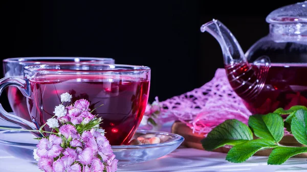 Hibiscus Red tea mug with carnation flowers close-up horizontal photo.English tea tradition.Medicinal therapy based on medicinal herbs and decoctions.Spicy herbs and medicinal broths.A relaxing drink