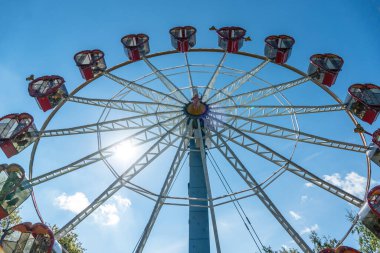 Mavi gökyüzünün arka planında kupa şeklinde kulübeleri olan dönme dolap. Atlıkarıncada romantik bir yürüyüş.
