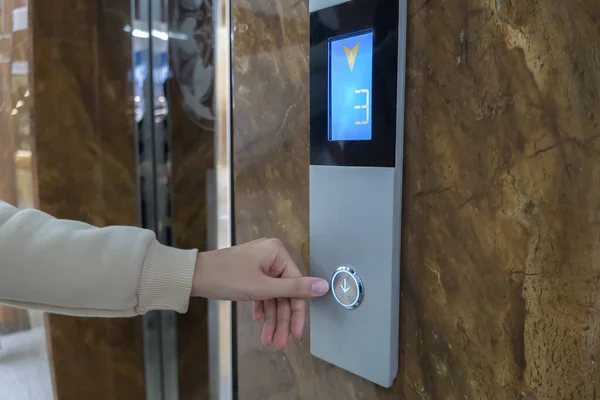 The girl calls the Elevator, ride the Elevator in the office, shopping center or business center to the second floor. The hand presses a button on the tableau with the numbers three 3