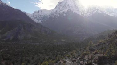 Manzaralı güneşli drone görüntüleri, kayalık nehir, mavi gökyüzünde karlı dağ zirveleri.