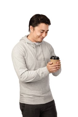 Kameraya bakarak çekici bir erkek gri hood gülümseyen forması giyen ve take-away kupa kahve Kupası holding beyaz bir arka plan karşı ayakta kendi 20s.