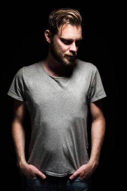 Karanlık bir odada siyah bir arkaplana karşı duran yoğun bakışlı sakallı bir adamın portresi..