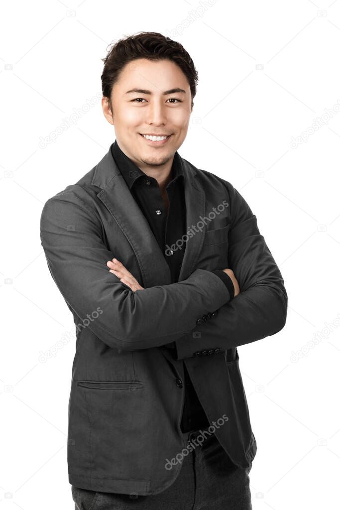 A good looking confident Asian guy smiling towards thecamera with his arms crossed wearing a black collared shirtunderneath a grey coat looking carefree alone against whitebackground.