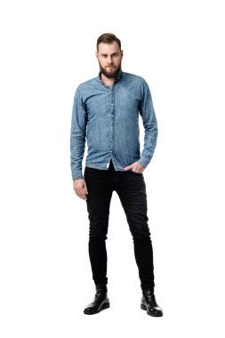 Bir eli cebinde, mavi uzun kollu bir gömlek giymiş kameraya bakarken ciddi görünen sakallı beyaz bir erkek resmi..