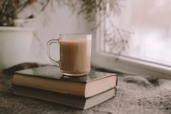 Coffee in transparent Cup is worth on books. Coffee, books and a blanket on the windowsill. Heart on the frozen window. A cozy winter day with coffee and books.