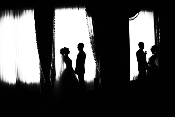 Silhouette of the bride and groom. Black and white photo. The bride and groom are reflected in the mirror. The bride and groom at the big window.