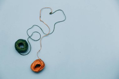 Renkli iplik bir kalp ile iç içedir. Örgü ve dikiş kavramı. Düğüm üzerinde mavi bir arka plan iş parçacığı.