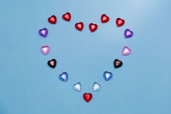 A big heart consisting of small multi-colored glass hearts on a blue background.