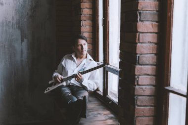 Yakışıklı adam müzisyen gitar çalmak. Bir tuğla duvar büyük pencerenin arka planda Loft uzayda gitarist