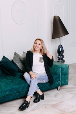 Parlak bir oda içinde kanepede oturan ve gülümseyen sarışın kadın