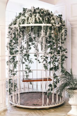 Büyük beyaz kafes çiçeklerle süslenmiş. Bir salıncak ve çiçekler ile kafes.