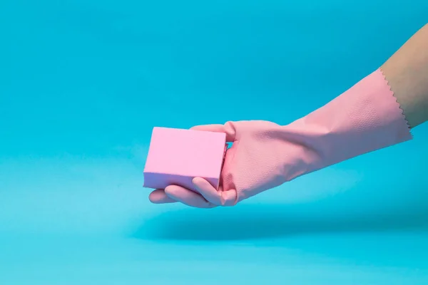 Mavi arka plan üzerinde pembe sünger ile pembe eldiven el.