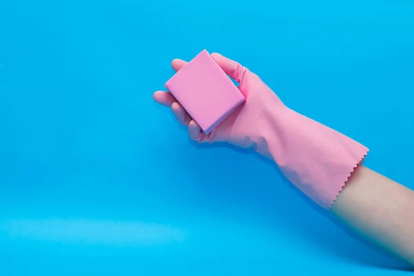 Hand in rosa Handschuh mit rosa Schwamm auf blauem Hintergrund. — Stockfoto