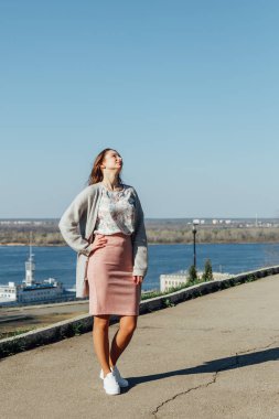 Güneşli bir günde köprüden şehir manzarasının tadını çıkaran uzun saçlı güzel kadın.