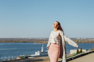 Güneşli bir günde köprüden şehir manzarasının tadını çıkaran uzun saçlı güzel kadın.