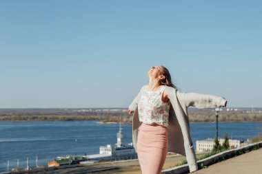 Güneşli bir günde köprüden şehir manzarasının tadını çıkaran uzun saçlı güzel kadın.