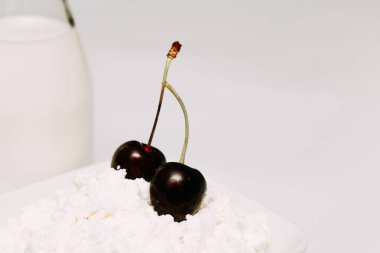 Beyaz bir arka plan üzerinde bir şişe süzme peynir ve kiraz çilek süt