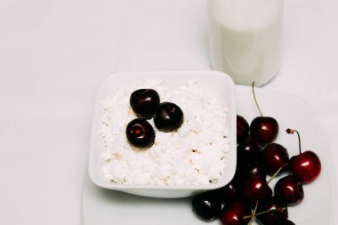 Beyaz bir arka plan üzerinde bir şişe süzme peynir ve kiraz çilek süt