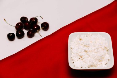 Kırmızı ve beyaz arka planda bir şişe süzme peynir ve kiraz çilek süt