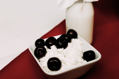 Kırmızı ve beyaz arka planda bir şişe süzme peynir ve kiraz çilek süt