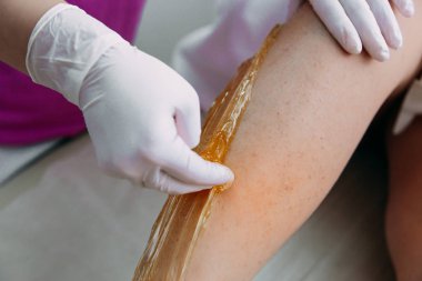 Genç bir kadın spa merkezinde sıvı şekerle bacakları tükürüyor.