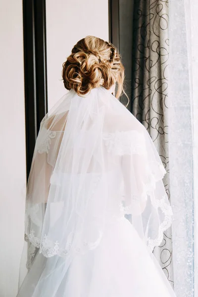 Noiva em vestido de noiva fica perto da janela, visão traseira — Fotografia de Stock