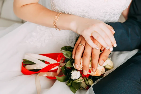 Mani con anelli sulle dita degli sposi sullo sfondo di un bouquet di nozze — Foto Stock
