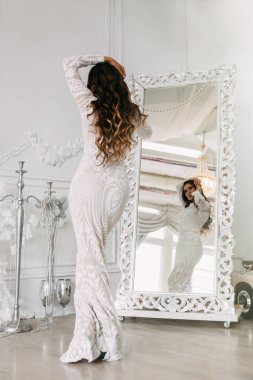 Beyaz elbiseli, genç, zayıf bir kadın aynanın karşısında dikiliyor..