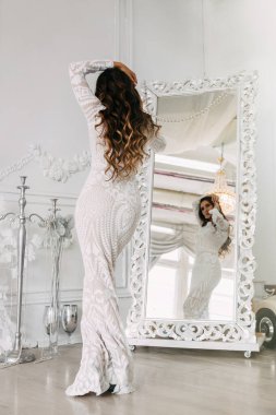 Beyaz elbiseli, genç, zayıf bir kadın aynanın karşısında dikiliyor..