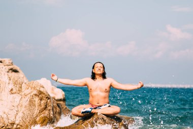 Denizde bir kayanın üzerinde meditasyon yapan adam..