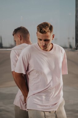 Şehir caddesinde cam ayna duvarına poz veren boş tişörtlü bir adam, model üzerinde ön t-shirt, şehir tarzı.