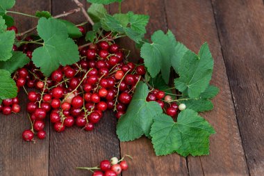 Olgun kırmızı üzümler, dallarında yeşil yapraklar olan siyah ahşap masa üzerinde uzanan.