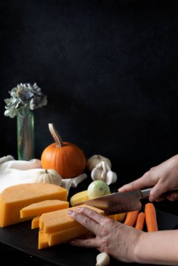 Balkabağı çorbası için renkli sonbahar sebzeleri, siyah arka planda balkabağı kesen kadın elleri, kopyalama alanı