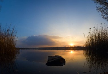 Gün batımı Arnavut kaldırımlı arkasında Nehri. Gün batımı arka planda bir baston bitki örtüsü. Su manzara akşam sakin.