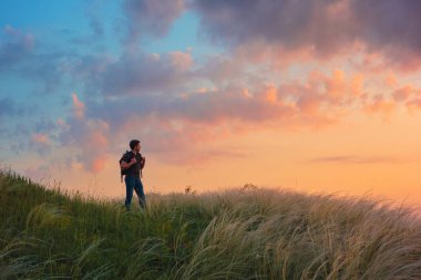 Kendinden emin gezgin alanında kalan ve gün batımı gökyüzüne bakıyor