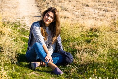 gri kazak ve kot bir çöl Türkmenistan çimenlerin üzerinde oturan genç bir kadın. Hafifçe gülümseyerek ve düz bir kameraya bakarak bir kadın 