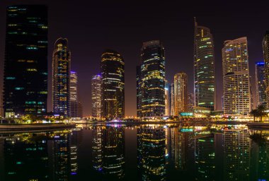 25 Ekim 2019; Jumeirah Lake Towers, Dubai, Birleşik Arap Emirlikleri; geceleri bir gölün yüzeyinde yansımaları olan gökdelenlerin manzarası. Yüksek çözünürlüklü panorama.