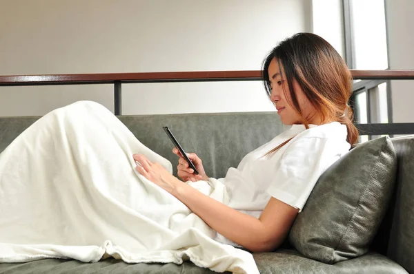 sick woman using smartphone on sofa