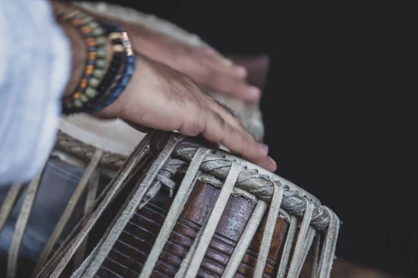 Image of a man\'s hands (wearing beads) playing the Tabla - Indian classical music percussion instrument - black background.