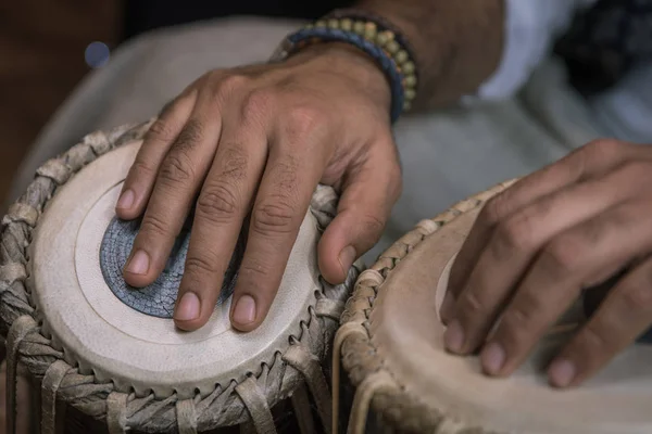Image of a man\'s hands (wearing beads) playing the Tabla - Indian classical music percussion instrument - black background.