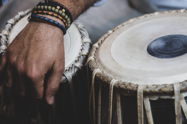 Image of a man's hands (wearing beads) playing the Tabla - Indian classical music percussion instrument - black background.