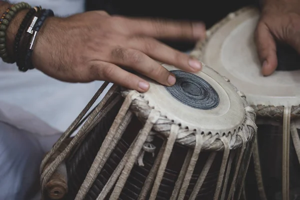 Image of a man's hands (wearing beads) playing the Tabla - Indian classical music percussion instrument - black background.