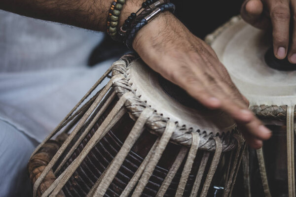 Image of a man's hands (wearing beads) playing the Tabla - Indian classical music percussion instrument - black background.