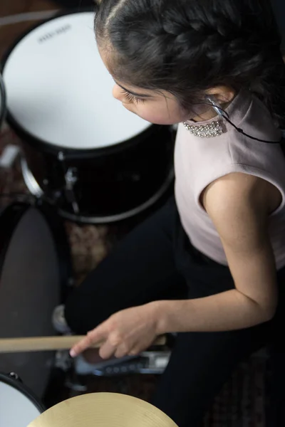 A 5 year old girl of British Indian ethnicity - practicing on the drums and reading music notes - on a dark black background.