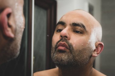 Bakım ve evde banyoda ayna önünde sakalını heykel bir kel, İngiliz Asya adam. O geleneksel kesme boğaz jilet ya da bir berber jilet kullanıyor. Bu tema sorunları maleness, dating ve orta yaş civarında için kullanılabilir. 